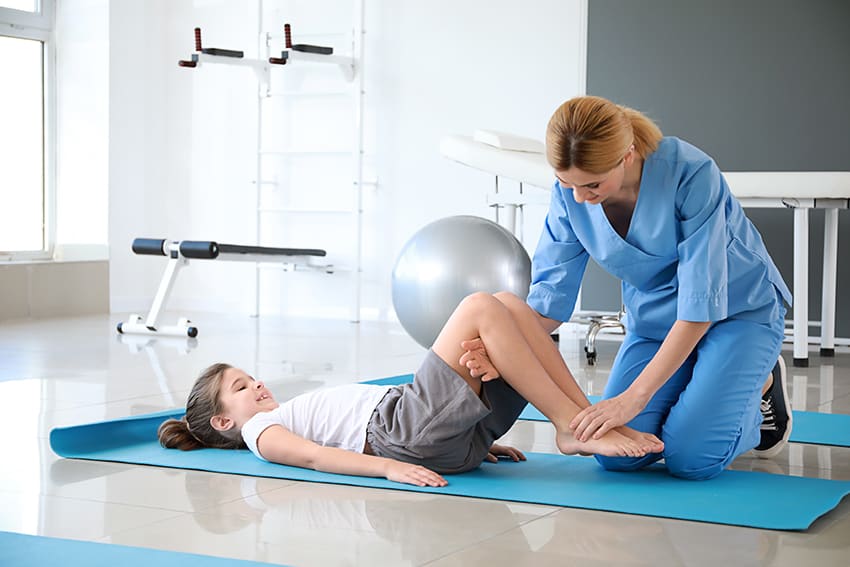 Kinderfysiotherapeut oefent met een kind op een mat met een gymbal