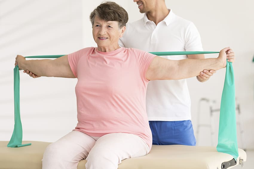 Fysiotherapeut begeleidt een vrouw bij een oefening met een elastische band